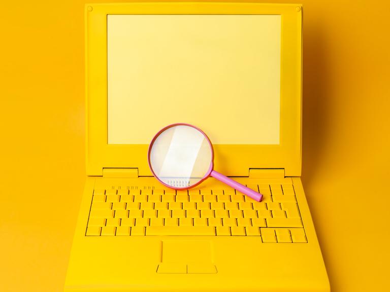 Ein gelber Laptop mit einer Lupe vor gelbem Hintergrund.