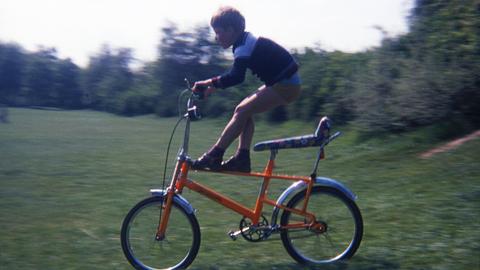 Ein Kind fährt mit einem orangenen Bonanza-Fahrrad über die Wiese.