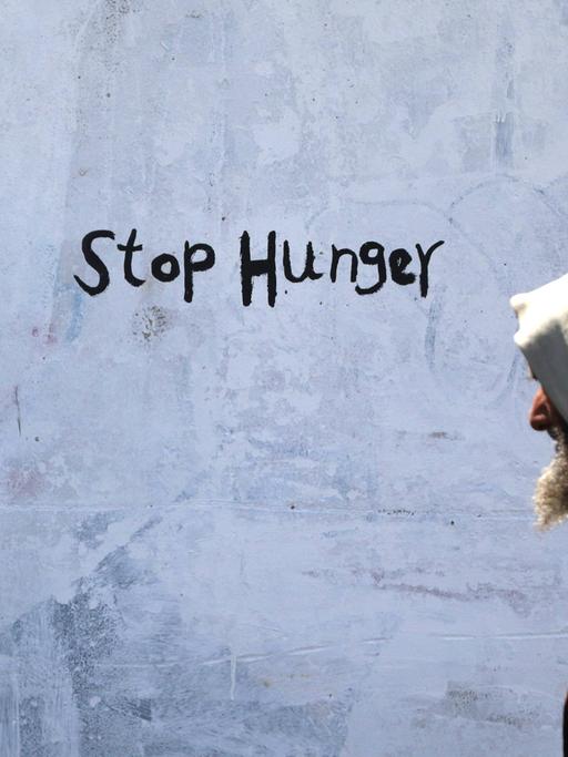 Ein älterer jemenitischer Mann geht an einer Hauswand vorbei, auf der "Stop Hunger" gesprüht ist.