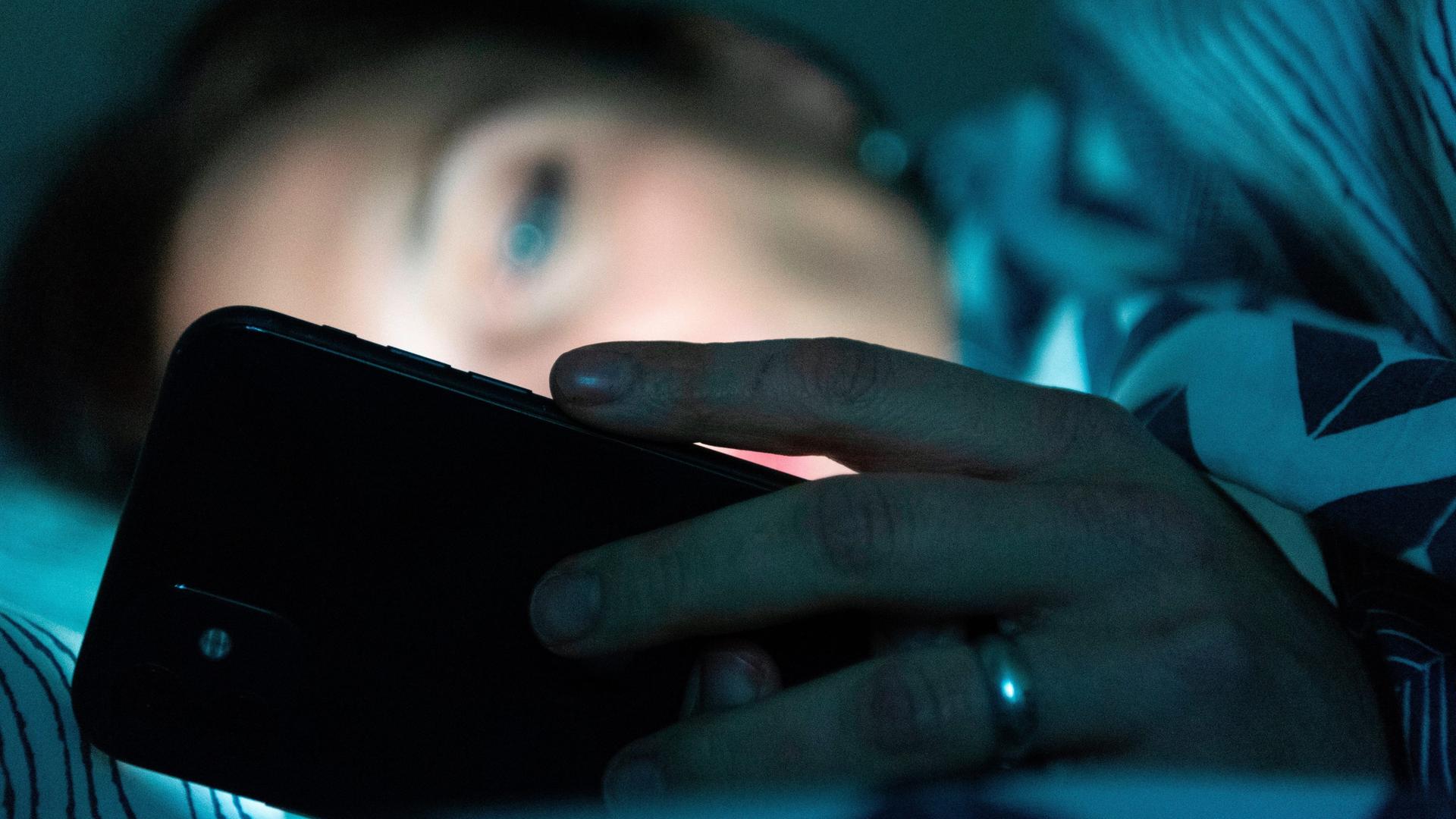 Eine Person liegt im Bett und schaut auf ein Smartphone. Eine Person liegt im Bett und schaut auf ein Smartphone.