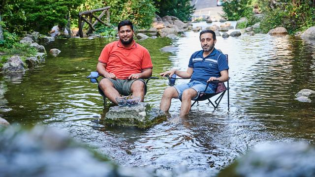 Um sich abzukühlen sitzen zwei Männer mit ihren Campingstühlen im einem Wasserbecken des Wasserfalls im Berliner Viktoriapark.
