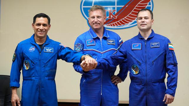 Die drei Raumfahrer stehen nahe beieinander und schütteln sich die Hände.