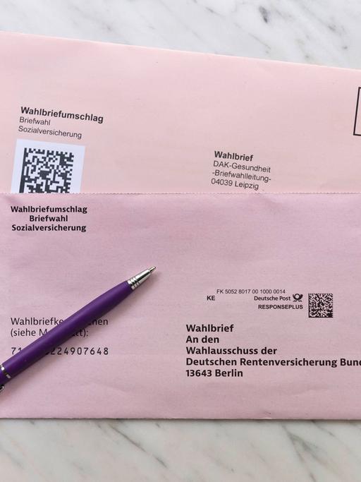 Zwei Briefe zur Sozialwahl 2023 liegen auf einem Marmortisch gemeinsam mit einem lila Kuli. 