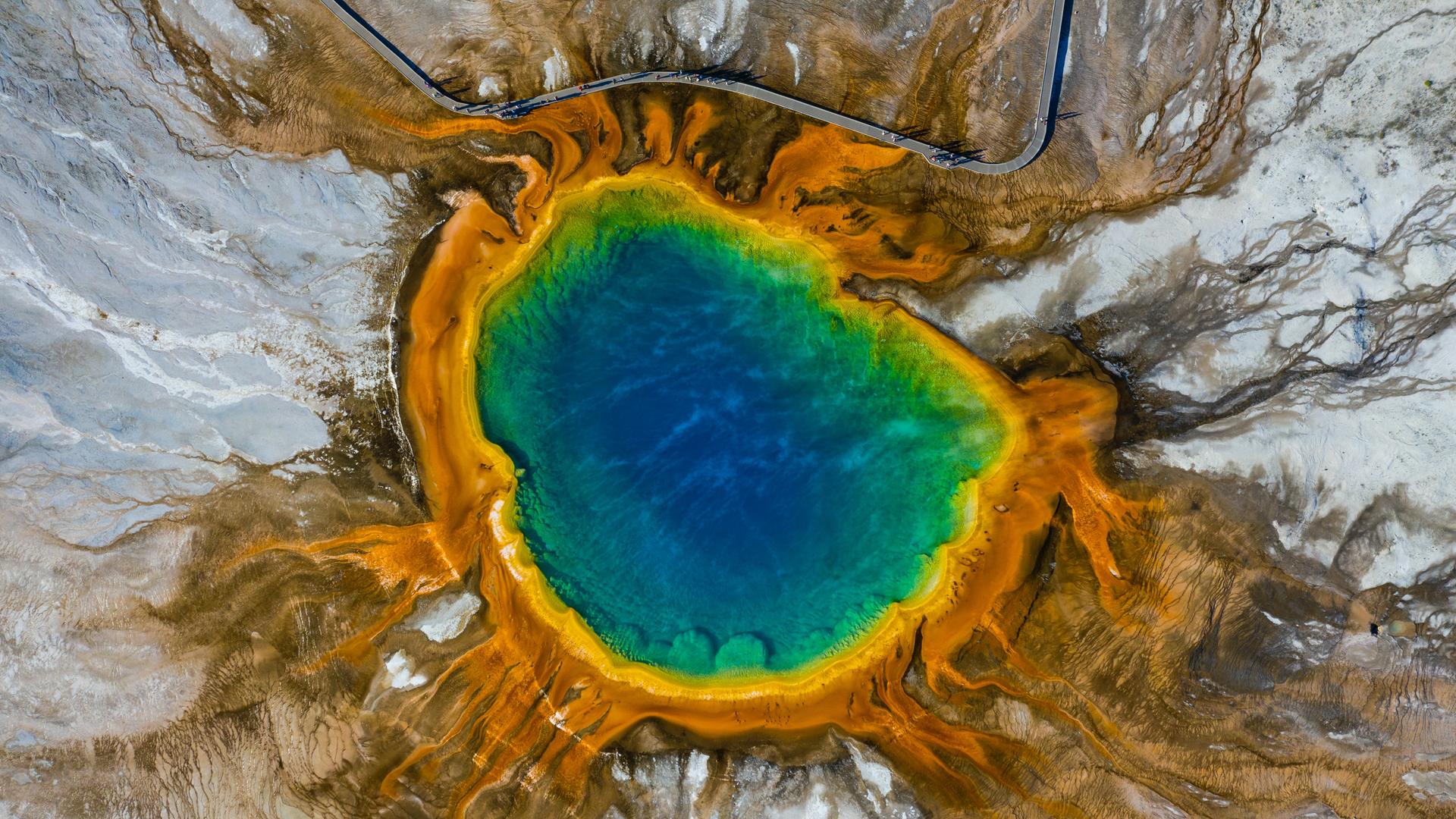 Aus der Luft aufgenommen: Ein knallblauer klarer See in felsiger Landschaft, die ihn einfasst - am Rand ist das Wasser eingefärbt mit verschiedenen Streifen in Regenbogenfarben. Aus der Luft aufgenommen: Ein knallblauer klarer See in felsiger Landschaft, die ihn einfasst - am Rand ist das Wasser eingefärbt mit verschiedenen Streifen in Regenbogenfarben.