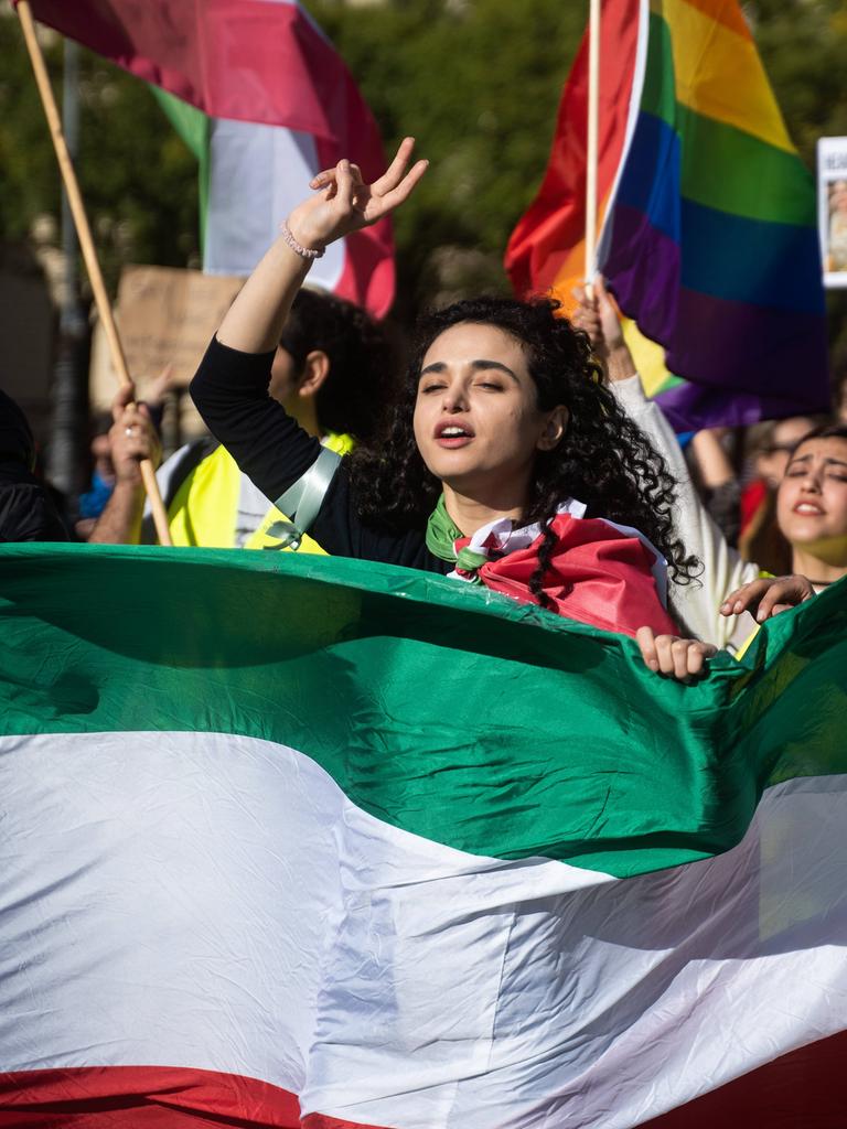 Protest für Mahsa Amini in München. Eine Teilnehmerin macht ein Peace Symbol. Im Vordergrund ist die Flagge des Iran zu sehen.