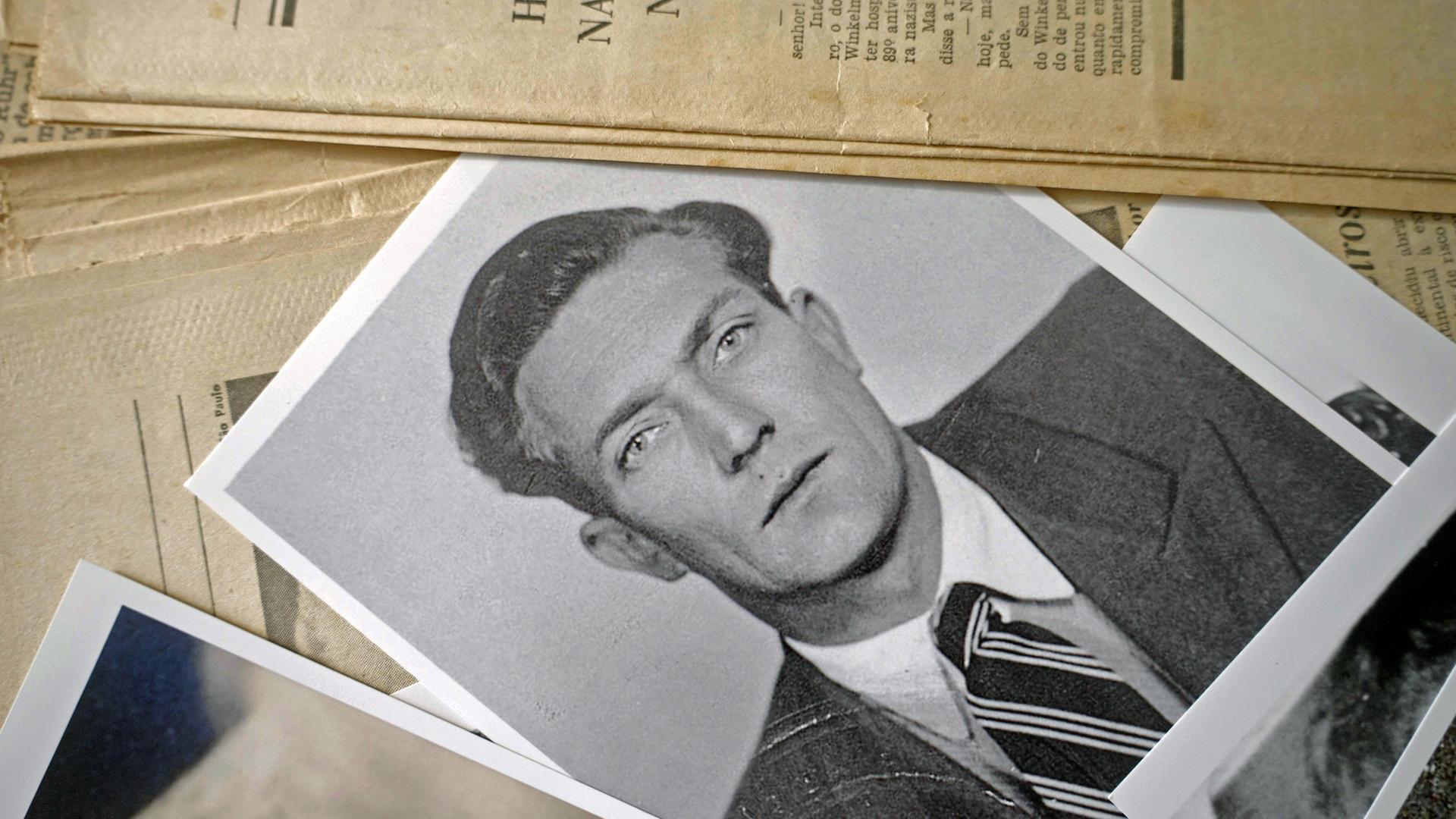 Die Schwarz-Weiß-Fotografie eines jungen Mannes – Gustav Wagner, SS-Aufseher im Vernichtungslagers Sobibór – liegt auf einem Tisch: Szene aus der ARD-Dokuserie "Shlomo - Der Goldschmied und der Nazi". Die Schwarz-Weiß-Fotografie eines jungen Mannes – Gustav Wagner, SS-Aufseher im Vernichtungslagers Sobibór – liegt auf einem Tisch: Szene aus der ARD-Dokuserie "Shlomo - Der Goldschmied und der Nazi".