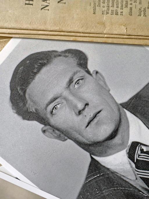 Die Schwarz-Weiß-Fotografie eines jungen Mannes –  Gustav Wagner, SS-Aufseher im Vernichtungslagers Sobibór – liegt auf einem Tisch: Szene aus der ARD-Dokuserie "Shlomo - Der Goldschmied und der Nazi". 