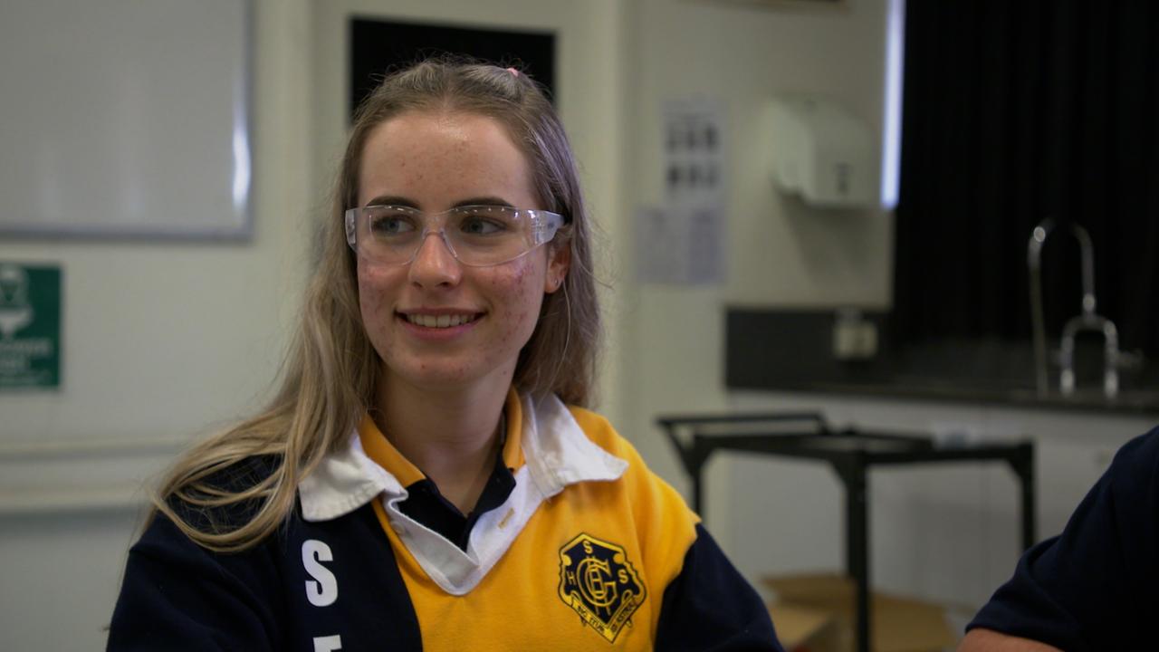 Ein junges Mädchen mit langen blonden Haaren sitzt in einem Sporttrikot in einem Klassenzimmer. Ein junges Mädchen mit langen blonden Haaren sitzt in einem Sporttrikot in einem Klassenzimmer.