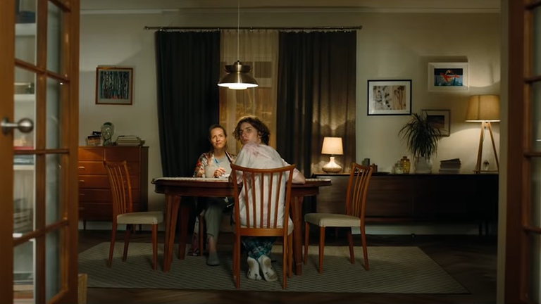 Auf dem Screenshot aus dem Werbevideo von Penny sieht man eine Mutter und ihren Teenagersohn am Wohnzimmertisch sitzen, der Sohn dreht sich um und blickt den Betrachter an und gleichzeitig in etwas Helles.