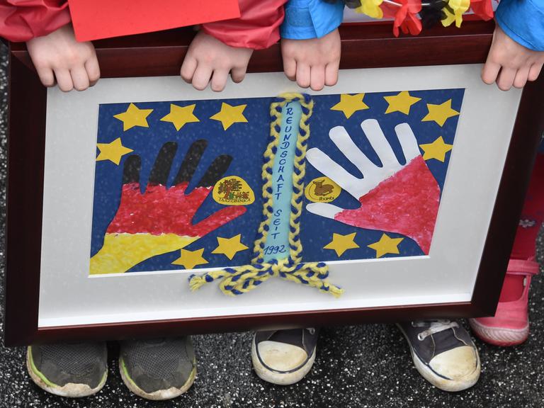 Zwei Kinder der Kita Bambi aus Frankfurt (Oder) halten ein selbst gemaltes Bild in einem Rahmen, das zwei Hände in den polnischen und deutschen Nationalfarben umringt von gelben Europasternen zeigt. 