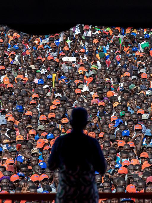 Silhouette eines Mannes, der vor einer großen Menschenmenge eine Rede hält.