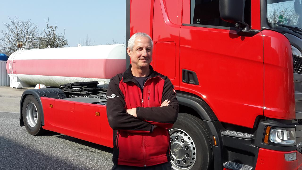 Ein Mann im roten Pullover steht mit verschränkten Armen vor einem roten LKW Ein Mann im roten Pullover steht mit verschränkten Armen vor einem roten LKW