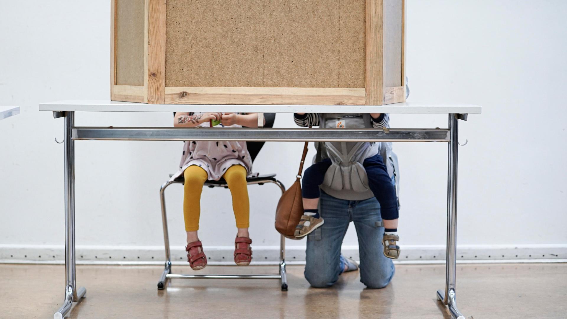 Eine Mutter hockt mit zwei Kindern in einer Wahlkabine. Eine Mutter hockt mit zwei Kindern in einer Wahlkabine.