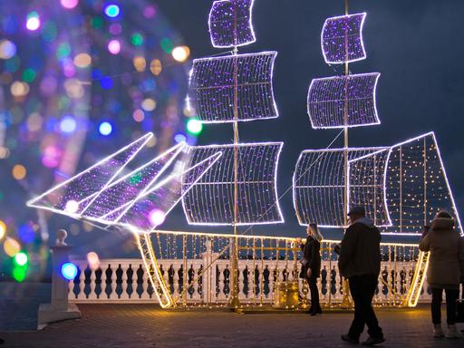 Bunte Lichter deuten am Meeresrand eine Schiffssilhouette an, die zu einer Weihnachtsbeleuchtung gehört.