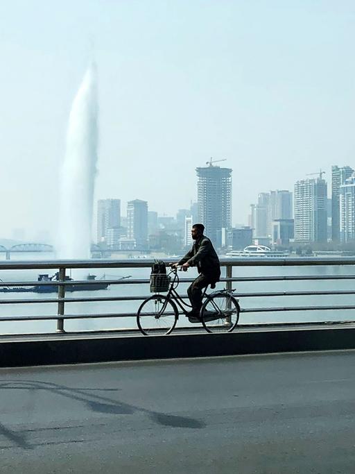 Ein Fahrradfahrer fährt über eine Brücke über den Taedong-Fluss in Pjöngjang. Im Hintergrund sind Hochhäuser zu sehen.