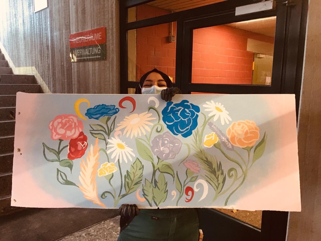 Fatemah hält ein Werkstück in der Hand, auf dem Blumen gezeichnet sind Fatemah hält ein Werkstück in der Hand, auf dem Blumen gezeichnet sind