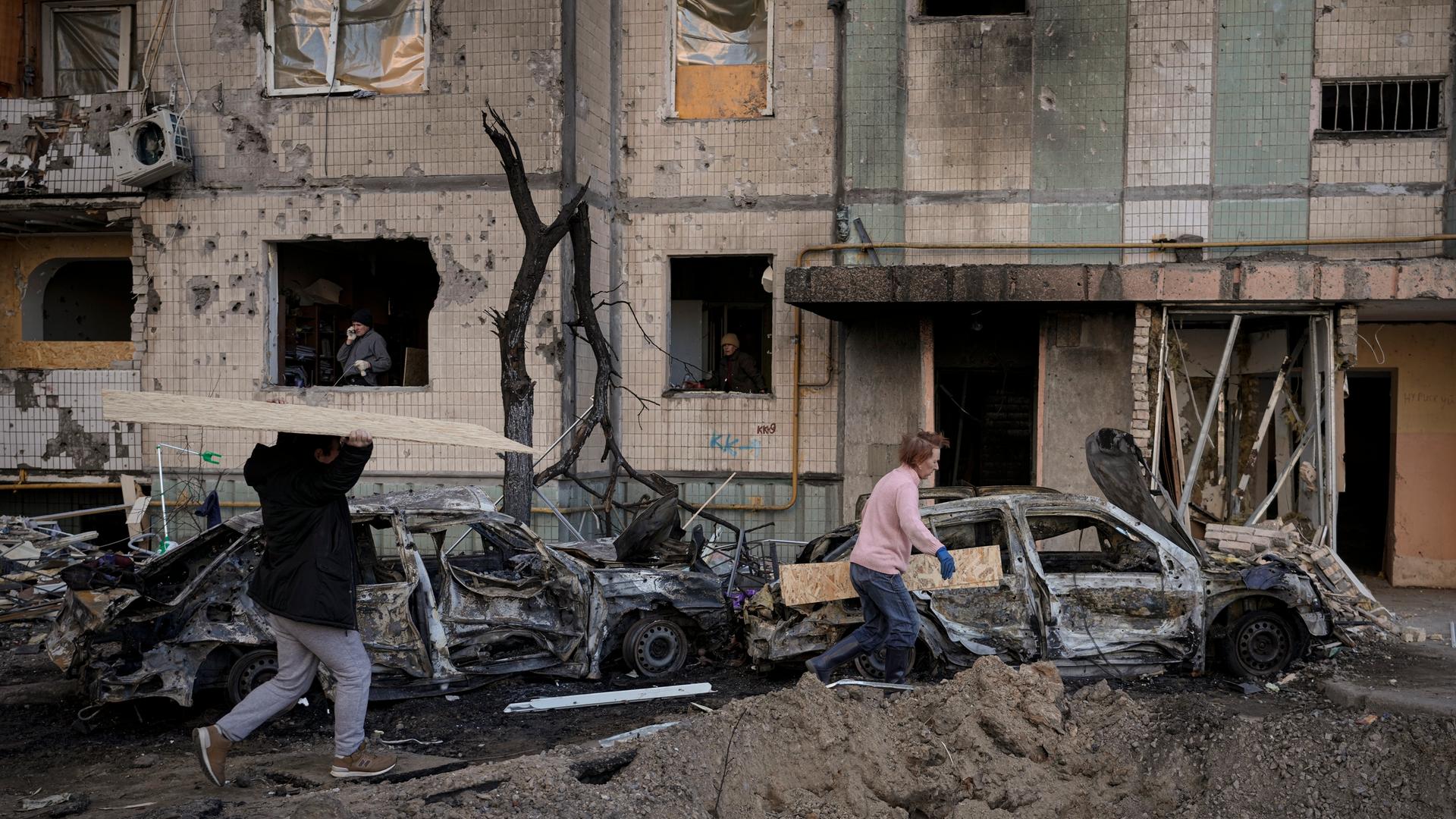 Menschen in Kiew tragen Holzbretter, um die Fenster eines Gebäudes abzudecken, das am Vortag bei einem Bombenangriff beschädigt wurde. Menschen in Kiew tragen Holzbretter, um die Fenster eines Gebäudes abzudecken, das am Vortag bei einem Bombenangriff beschädigt wurde.