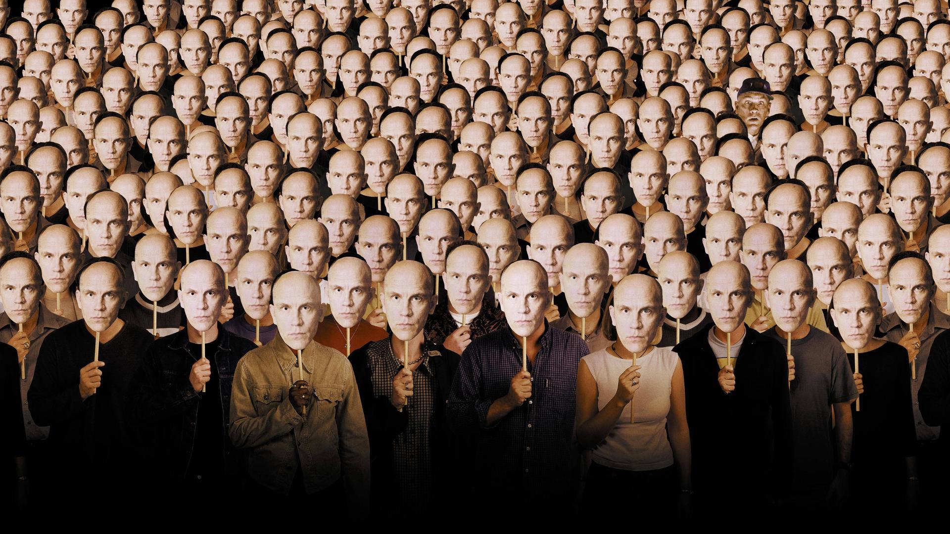 Im Filmbild aus "Being John Malkovich" stehen viele Menschen nebeneinander und halten sich Pappmasken vor die eigenen Gesichter, die alle das Gesicht von John Malkovich zeigen. Im Filmbild aus "Being John Malkovich" stehen viele Menschen nebeneinander und halten sich Pappmasken vor die eigenen Gesichter, die alle das Gesicht von John Malkovich zeigen.