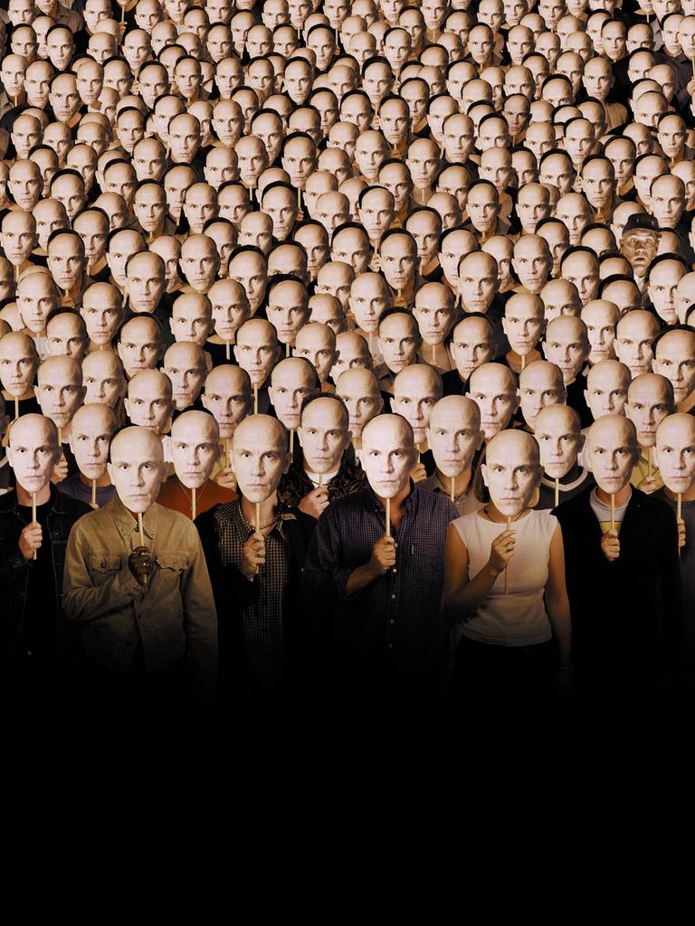 Im Filmbild aus "Being John Malkovich" stehen viele Menschen nebeneinander und halten sich Pappmasken vor die eigenen Gesichter, die alle das Gesicht von John Malkovich zeigen.