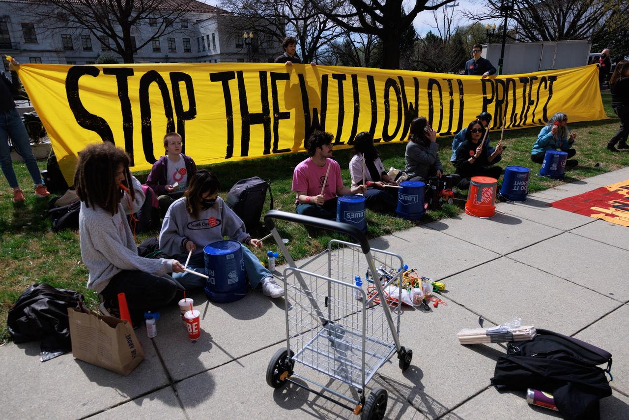 Menschen sitzen vor einem Banner mit der Aufschrift "Stop the Willow oil project". Menschen sitzen vor einem Banner mit der Aufschrift "Stop the Willow oil project".