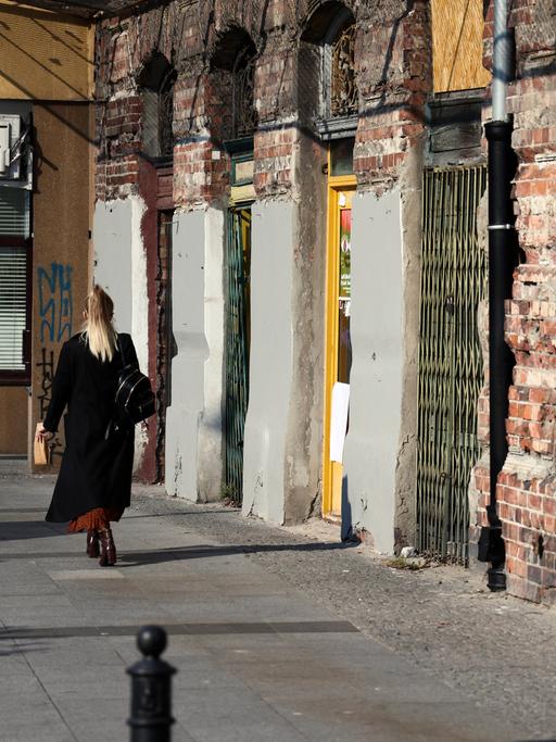Warschauer Alltagsszene: Eine Frau geht auf dem Gehsteig an einem alten, unverputzten Mietshaus vorbei