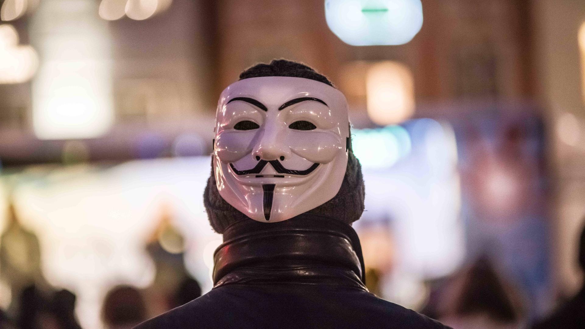 Ein Mann trägt auf dem Hinterkopf eine Maske des Anonymous. Ein Mann trägt auf dem Hinterkopf eine Maske des Anonymous.