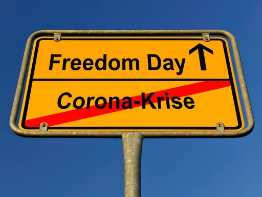 Ein Schild ist zu sehen, auf dem "Corona-Krise" durchgestrichen, darüber steht "Freedom Day".
