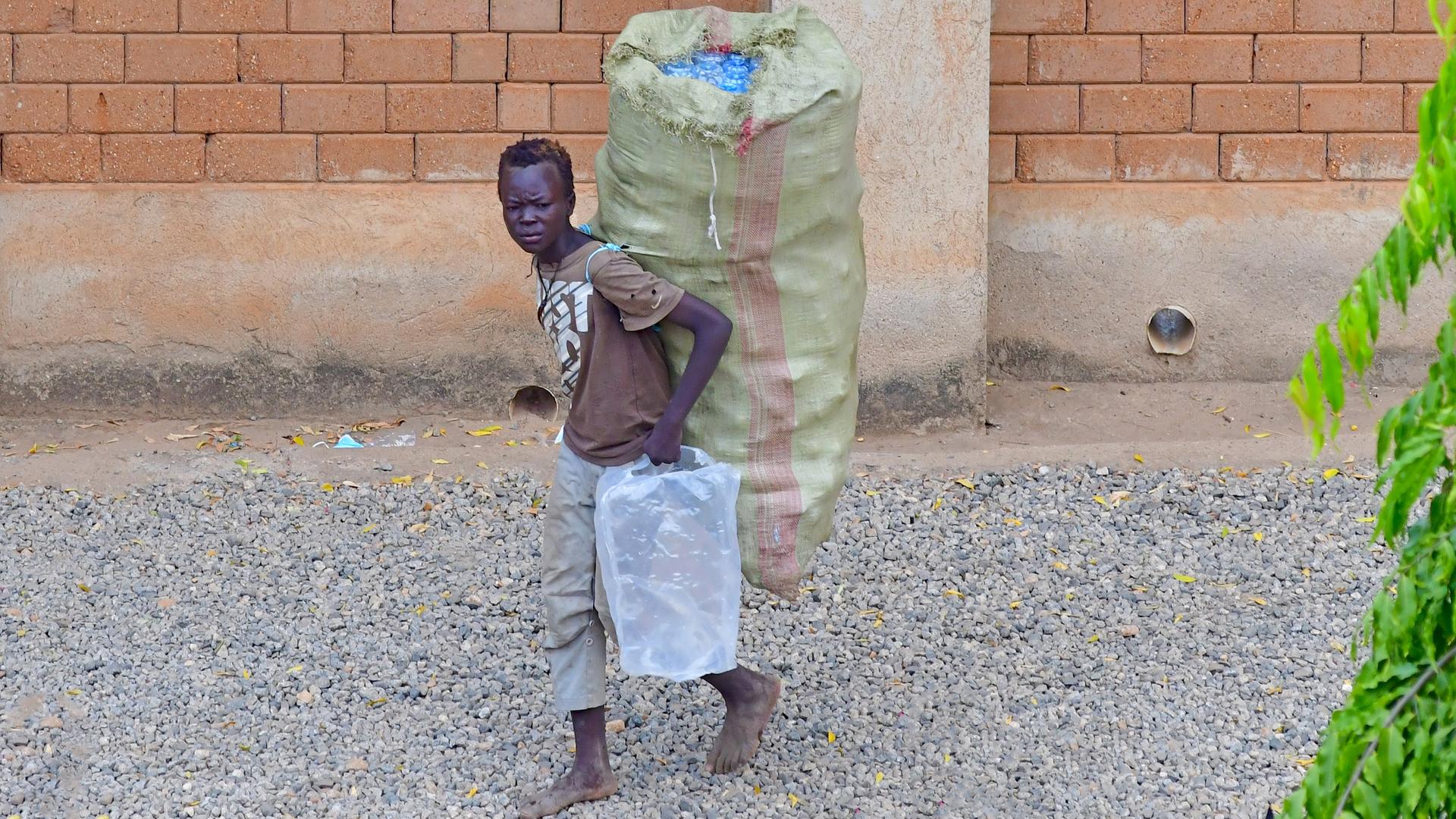 Ein Junge im Südsudan trägt eingesammelte Plastikflaschen in Taschen zu einer Annahmestelle, wo das Plastik wiederverwertet wird, und er für seine Sammlung einen geringen Geldbetrag erhält, aufgenommen am 13.06.2021. Ein Junge im Südsudan trägt eingesammelte Plastikflaschen in Taschen zu einer Annahmestelle, wo das Plastik wiederverwertet wird, und er für seine Sammlung einen geringen Geldbetrag erhält, aufgenommen am 13.06.2021.