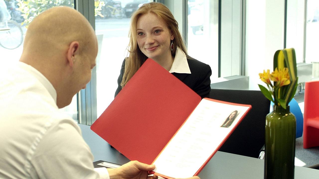 Eine attraktive junge Frau sitzt bei einem Bewerbungsgespräch einem kahlköpfigen Personaler gegenüber, der in ihre Bewerbungsmappe schaut (Stockfoto/Symbolfoto) Eine attraktive junge Frau sitzt bei einem Bewerbungsgespräch einem kahlköpfigen Personaler gegenüber, der in ihre Bewerbungsmappe schaut (Stockfoto/Symbolfoto)