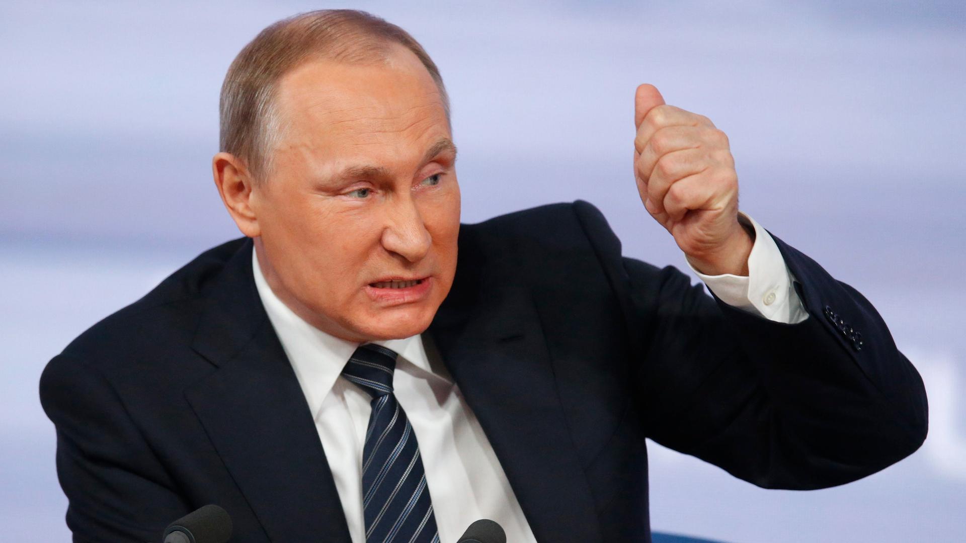 Porträt von Wladimir Putin vor zwei Mikrofonen. Er guckt böse, während er spricht und hat die Faust erhoben, als wolle er damit auf den Tisch hauen. Porträt von Wladimir Putin vor zwei Mikrofonen. Er guckt böse, während er spricht und hat die Faust erhoben, als wolle er damit auf den Tisch hauen.