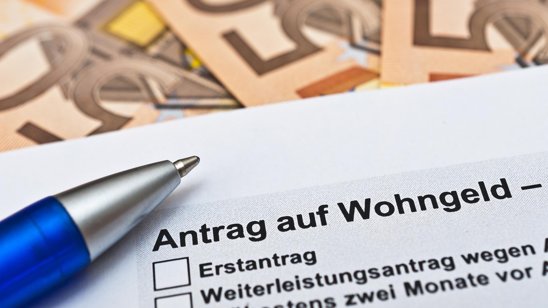 Zu sehen ist ein Stift auf einem Wohngeld-Antrag, darunter liegen symbolhaft Geldscheine. Zu sehen ist ein Stift auf einem Wohngeld-Antrag, darunter liegen symbolhaft Geldscheine.