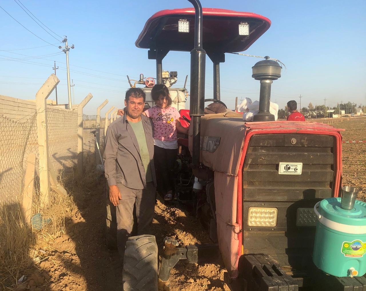 Auf dem staubigen, roten Traktor im Feld steht das Mädchen Lana in pinkem T-Shirt. Neben ihr der Vater und Landwirt in grauer Hose und mit der Sonne im Gesicht.