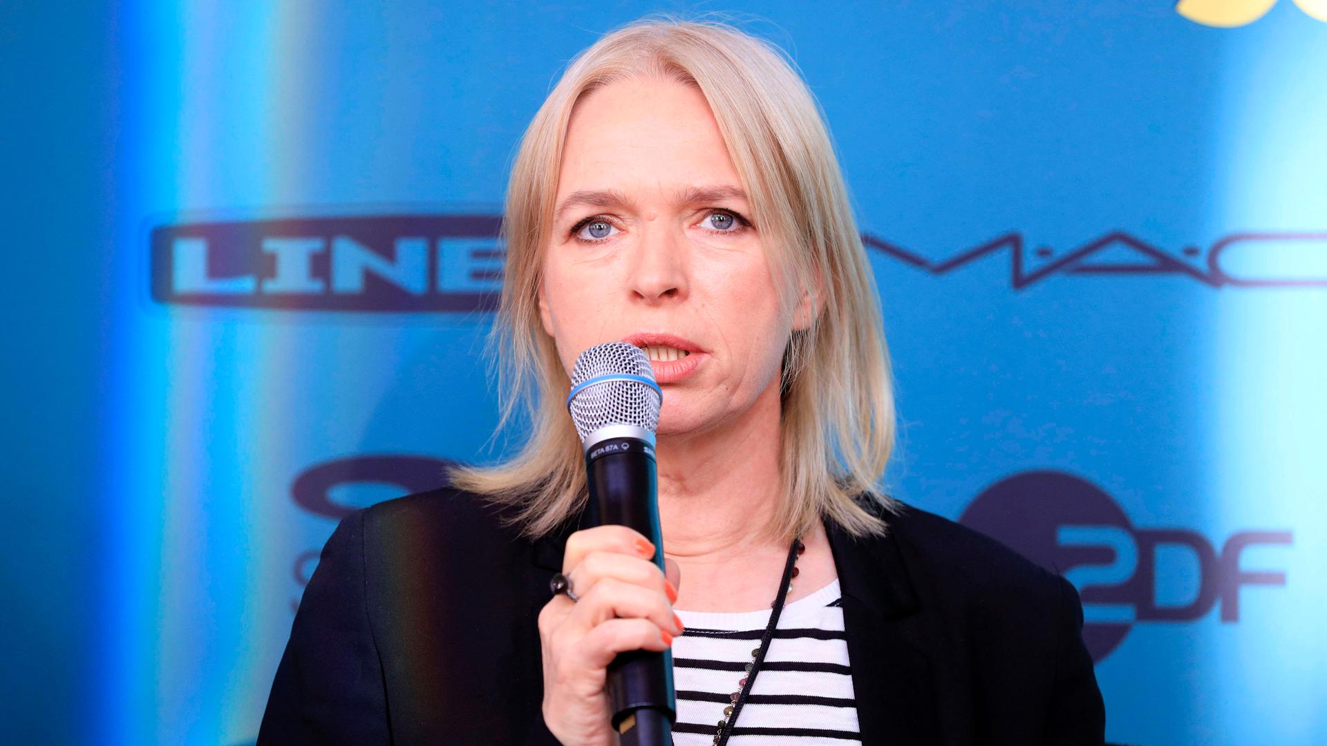 Annette Hess spricht auf einem Podium in ein Mikrofon. Annette Hess spricht auf einem Podium in ein Mikrofon.