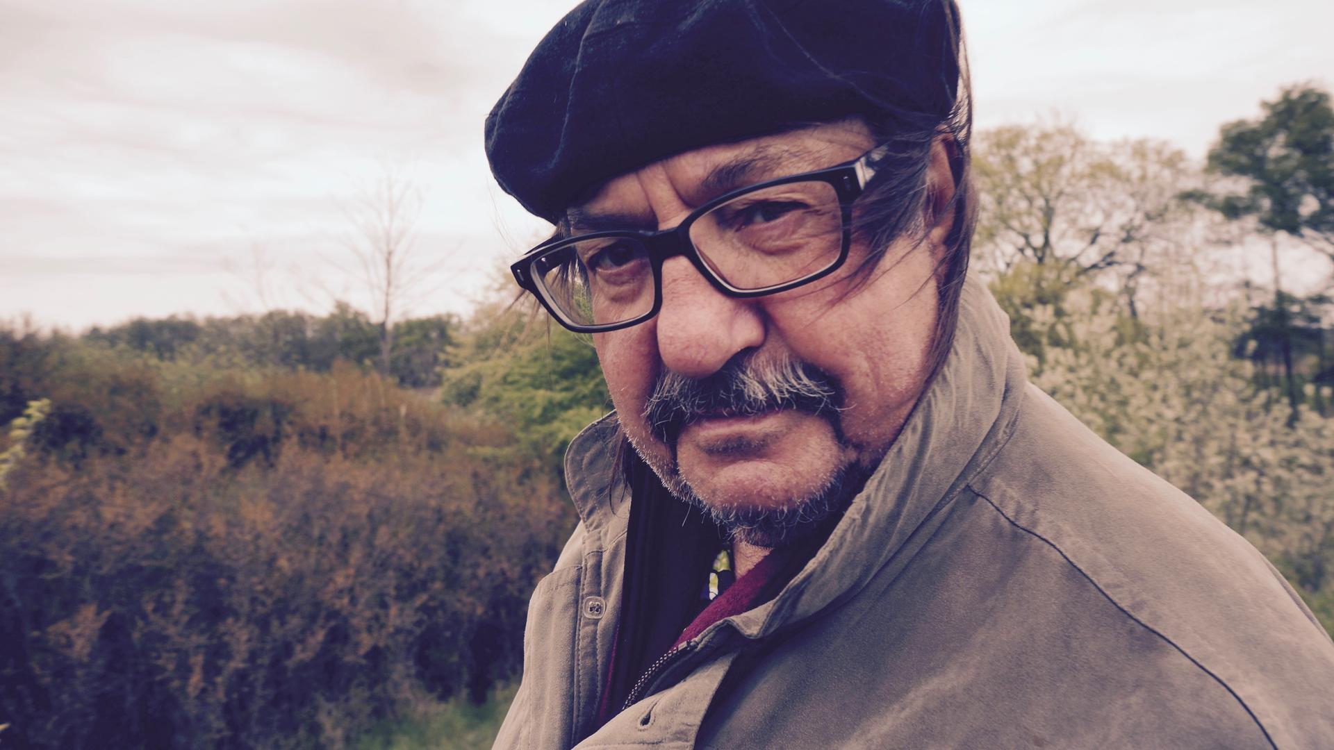 Der Autor und Liedermacher Manfred Maurenbrecher trägt Brille und Mütze und steht in der Natur. Der Wind bläst ihm die Haare ins Gesicht. Der Autor und Liedermacher Manfred Maurenbrecher trägt Brille und Mütze und steht in der Natur. Der Wind bläst ihm die Haare ins Gesicht.