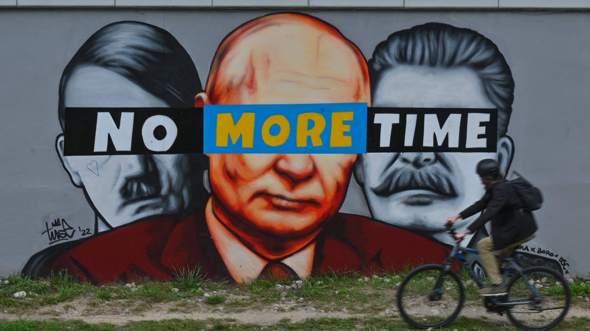 Ein Fahrradfahrer fährt in Gdansk an einer Mauer vorbei, auf die der polnische Künstler Piotr TUSE Jaworski die Konterfeis von HItler, Putin und Stalin gesprayt hat mit einem Banner mit der Aufschrift "No more time" über den Augen.