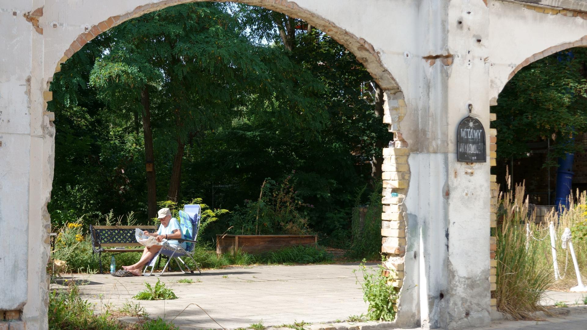 Ein Rentner sitzt auf einem Gartenstuhl und liest Zeitung. Man sieht ihn durch einen ausgefranzten Torbogen durch. Ein Rentner sitzt auf einem Gartenstuhl und liest Zeitung. Man sieht ihn durch einen ausgefranzten Torbogen durch.