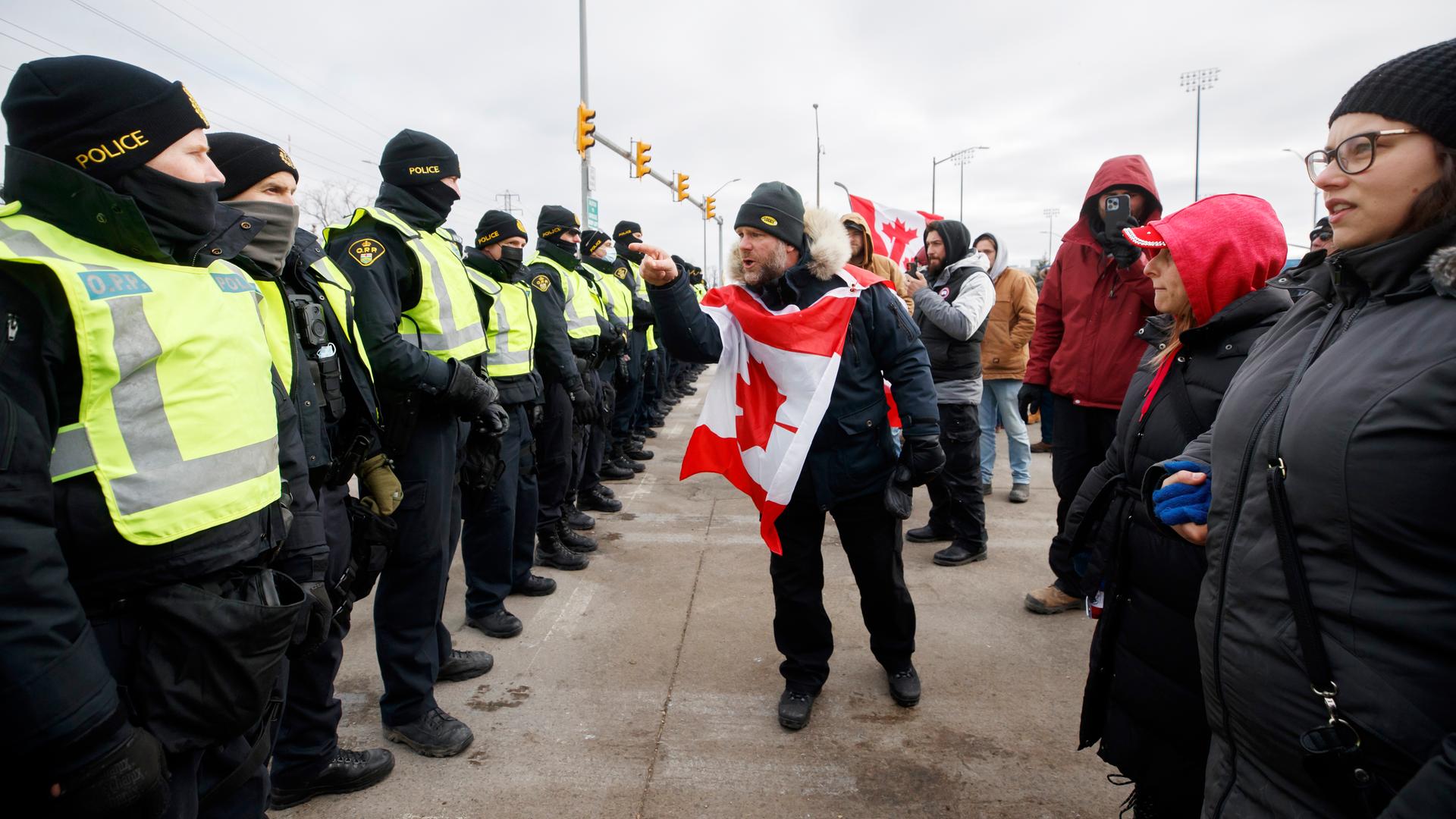 Protestblockade in Kanada, ein Mann aus der Menschenmenge mit kanadischer Flagge um den Hals schreit die Polizeibeamten an, 12. Februar 2022.
