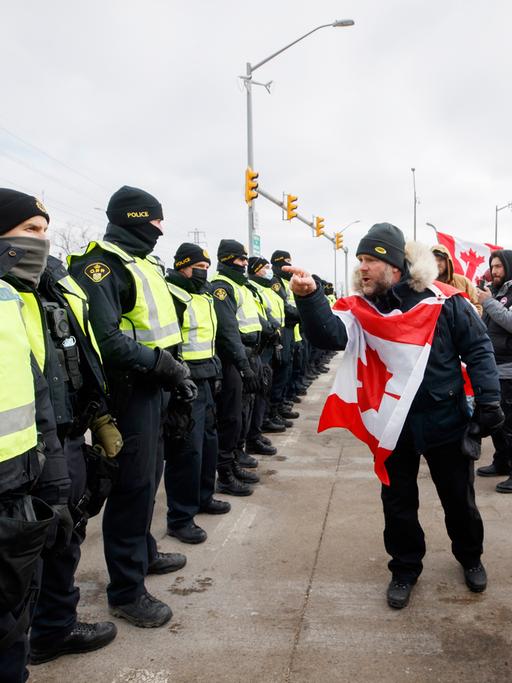 Protestblockade in Kanada, ein Mann aus der Menschenmenge mit kanadischer Flagge um den Hals schreit die Polizeibeamten an, 12. Februar 2022.