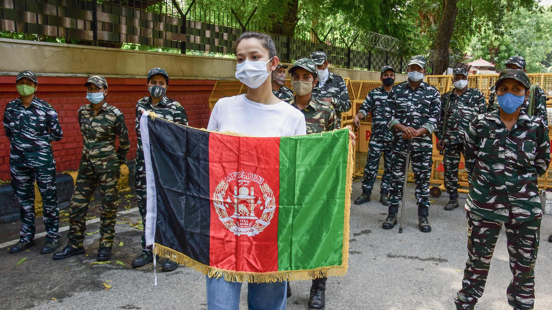 Eine junge Frau, die von indischen Polizistinnen umringt wird, hält eine afghanische Flagge vor sich in die Höhe. Eine junge Frau, die von indischen Polizistinnen umringt wird, hält eine afghanische Flagge vor sich in die Höhe.