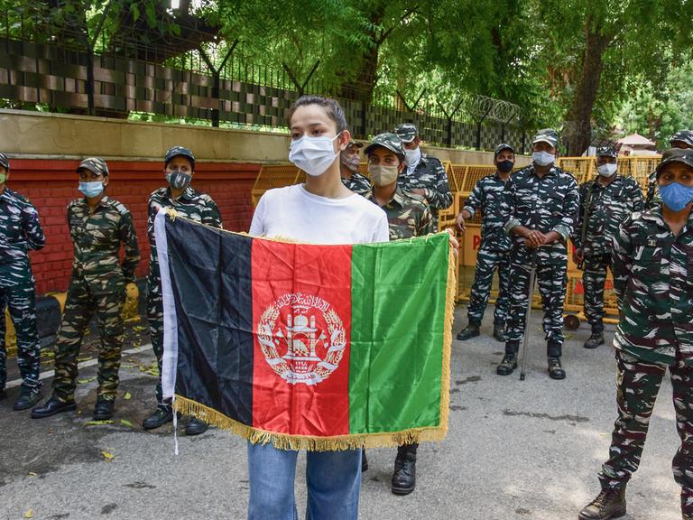 Eine junge Frau, die von indischen Polizistinnen umringt wird, hält eine afghanische Flagge vor sich in die Höhe.
