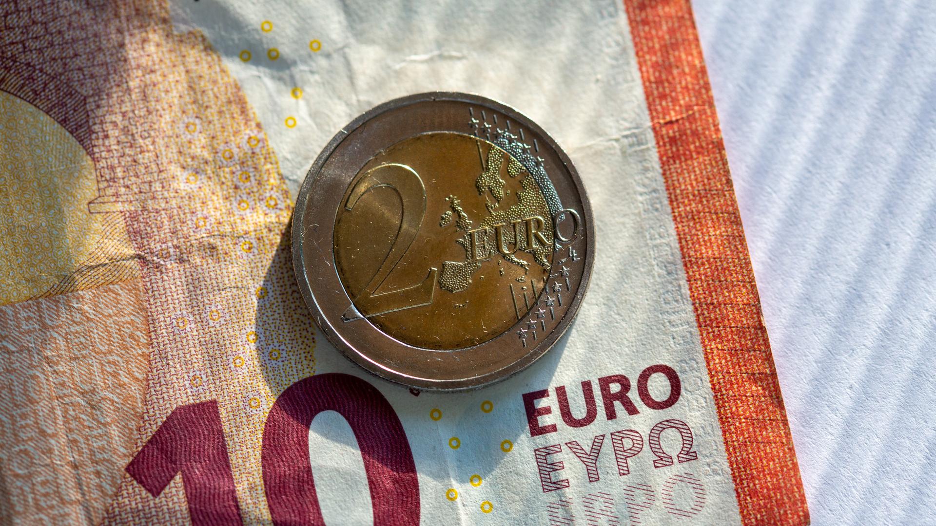 Ein Zehn-Euro-Schein und eine Zwei-Euro-Münze liegen auf einem Tisch.