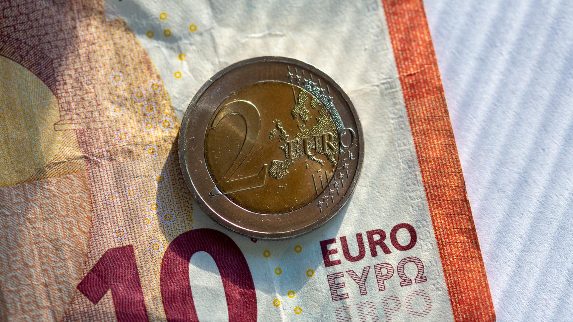 Ein Zehn-Euro-Schein und eine Zwei-Euro-Münze liegen auf einem Tisch. Ein Zehn-Euro-Schein und eine Zwei-Euro-Münze liegen auf einem Tisch.
