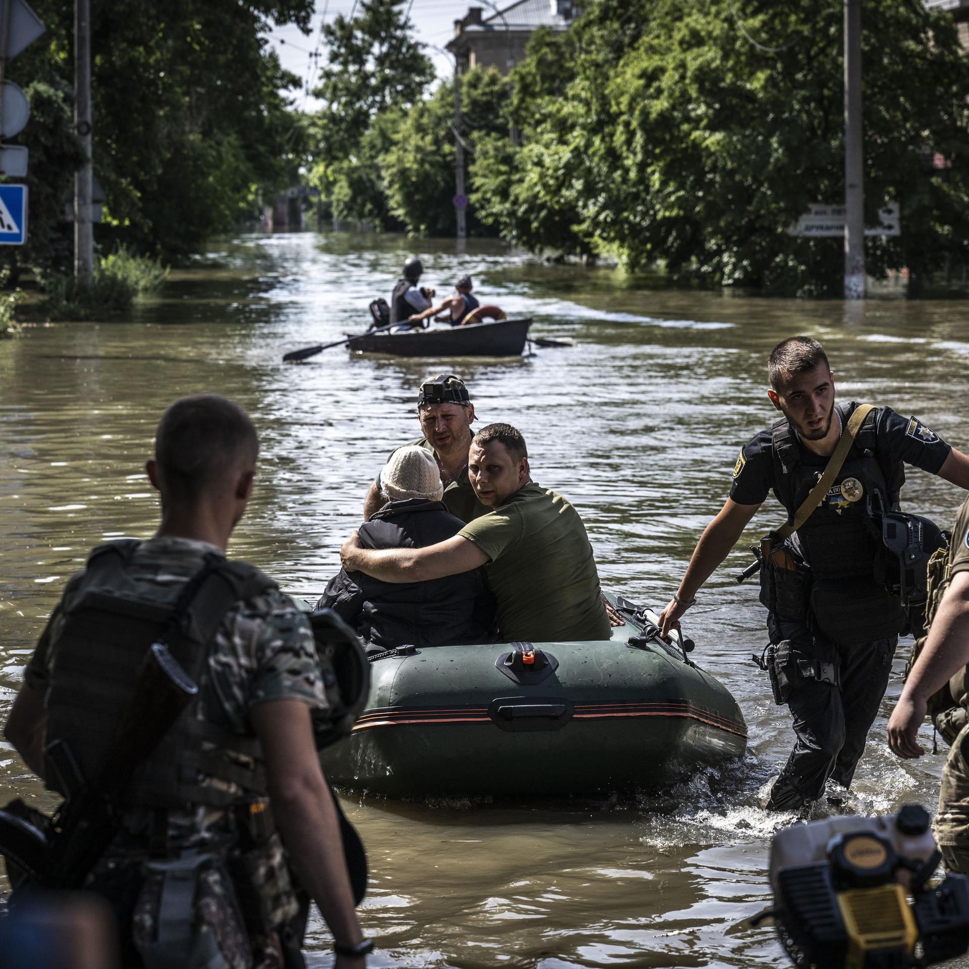 Menschen werden aus überschwemmten Gebieten evakuiert, nachdem die Explosion im Wasserkraftwerk Kachowka am 7. Juni 2023 in Cherson, Ukraine, zu Überschwemmungen geführt hat. Zu sehen ist eine überflutete Straße mit Zivilisten in Schlauchbooten und Soldaten, die Hilfe leisten.