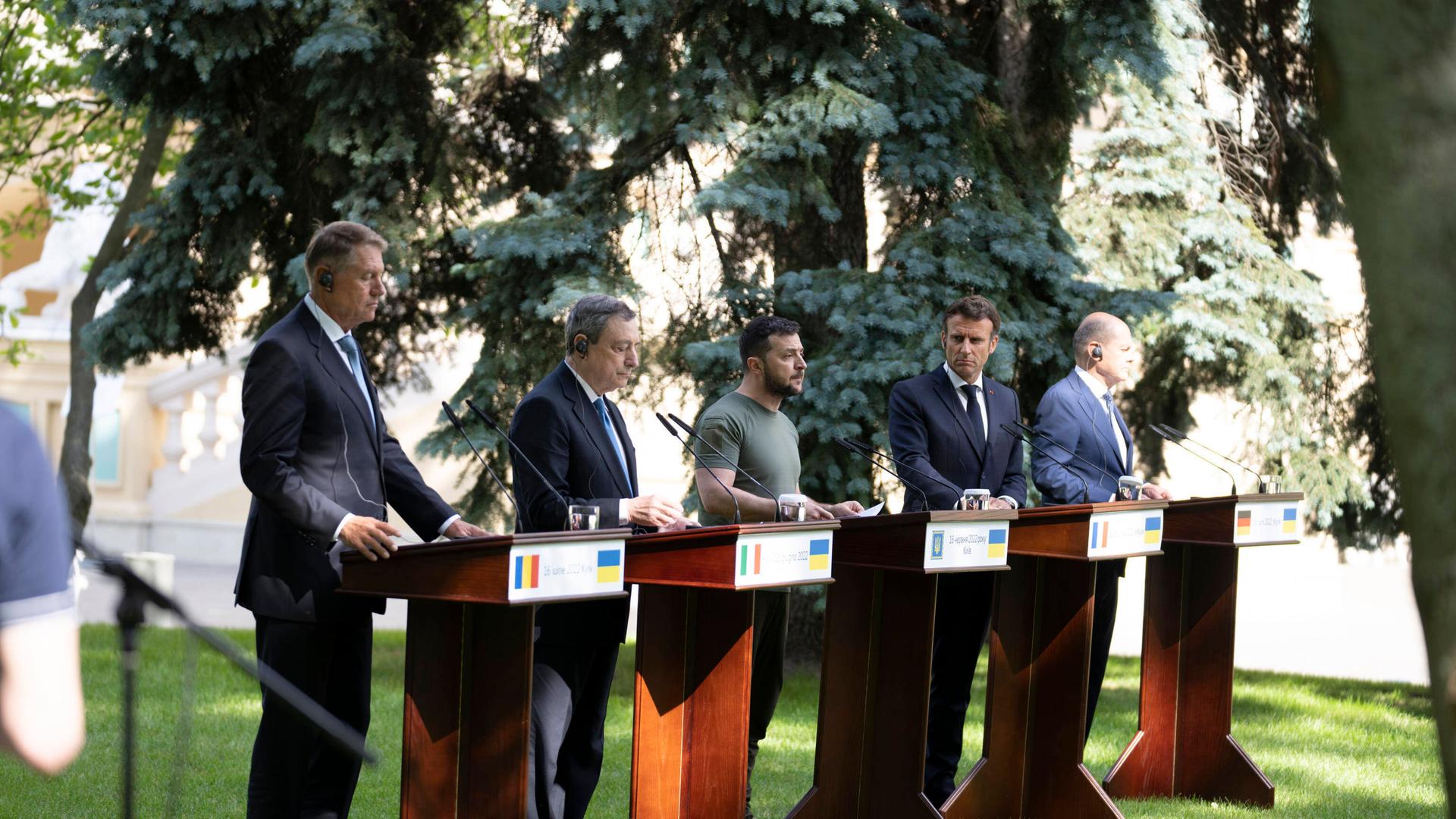 Fünf Männer stehen in einem Garten vor Rednerpulten und geben eine Pressekonferenz. Fünf Männer stehen in einem Garten vor Rednerpulten und geben eine Pressekonferenz.