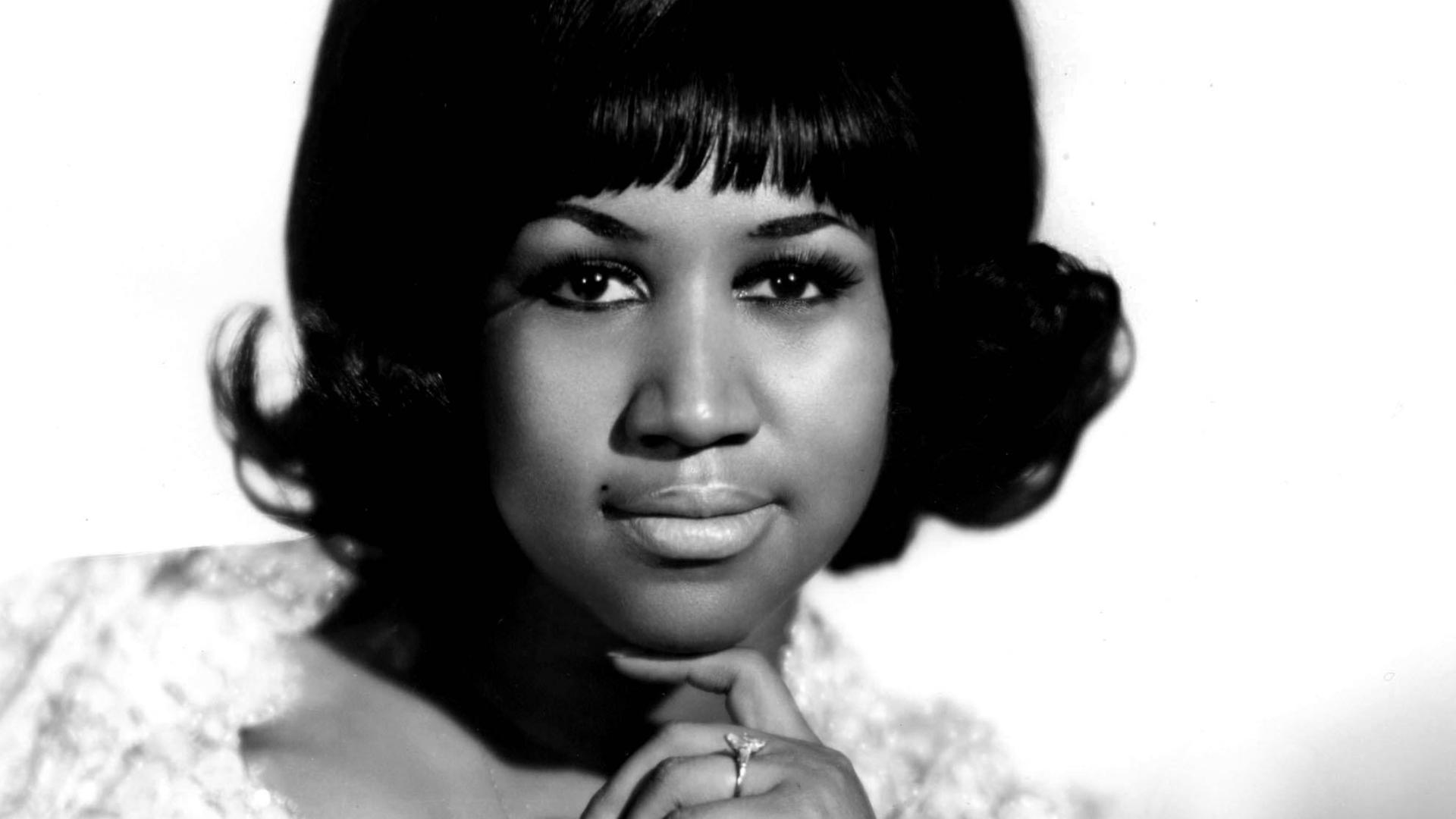 Aretha Franklin, die Queen of Soul, mit einem weißen Kleid auf einem Stuhl sitzend. Sie schaut in die Kamera. Aretha Franklin, die Queen of Soul, mit einem weißen Kleid auf einem Stuhl sitzend. Sie schaut in die Kamera.