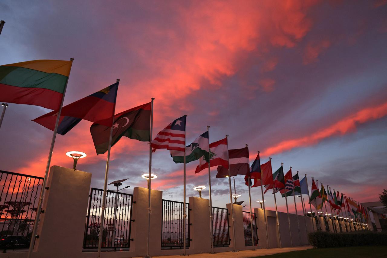 Die Flaggen der Länder der Vereinten Nationen stehen aufgereiht nebeneinander und wehen vor einem glühenden Abendhimmel.