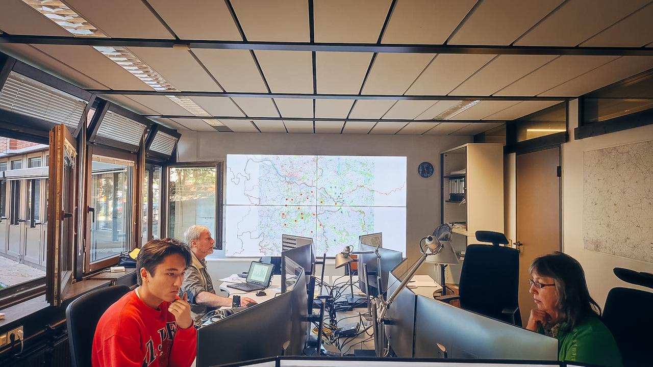 Blick in den Arbeitsraum der Waldbrandzentrale Lüneburg. Drei Personen sitzen vor Computern. Im Hintergrund eine digitale Karte an der Wand.