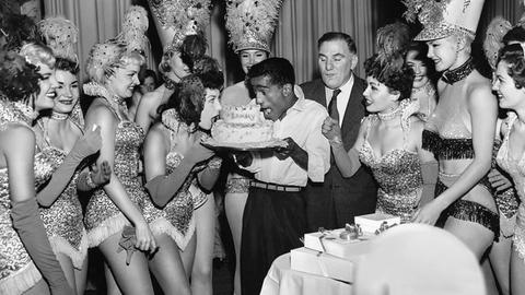 Sammy Davis Jr. & glitzernde Showgirls bei einer Pemiere in Las Vegas mit einer Torte auf der "Sammy" steht, 1955.