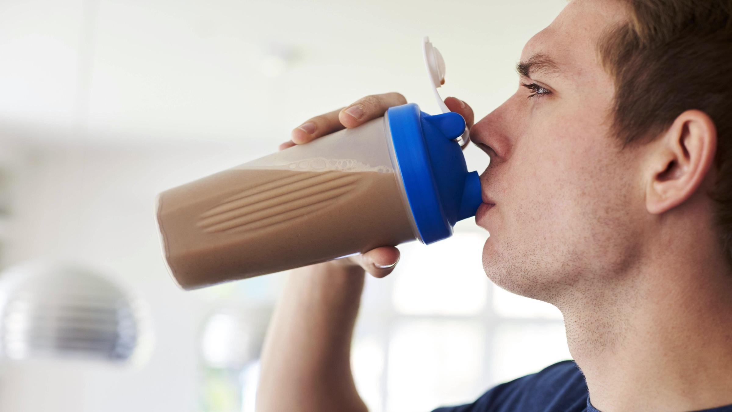 Ein junger Mann trinkt einen Protein Shake aus seiner Sportflasche.