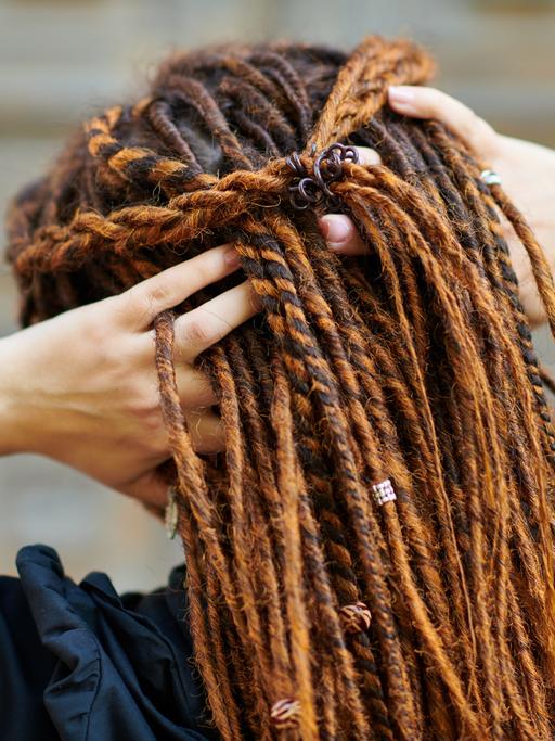 Eine weiße Frau fasst sich am Hinterkopf in ihre Dreadlocks. 
